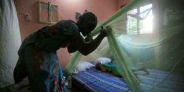 Nainen levittää moskiittoverkkoa lapsensa vuoteen ylle Norsunluurannikon Abidjanissa.