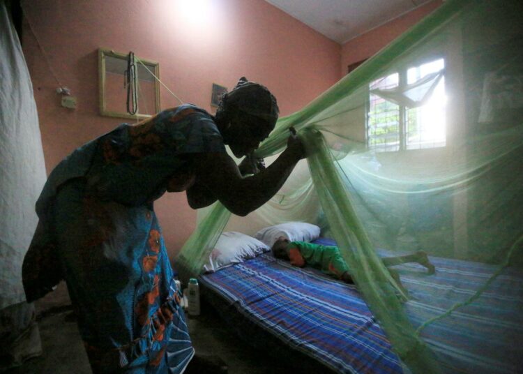 Nainen levittää moskiittoverkkoa lapsensa vuoteen ylle Norsunluurannikon Abidjanissa.