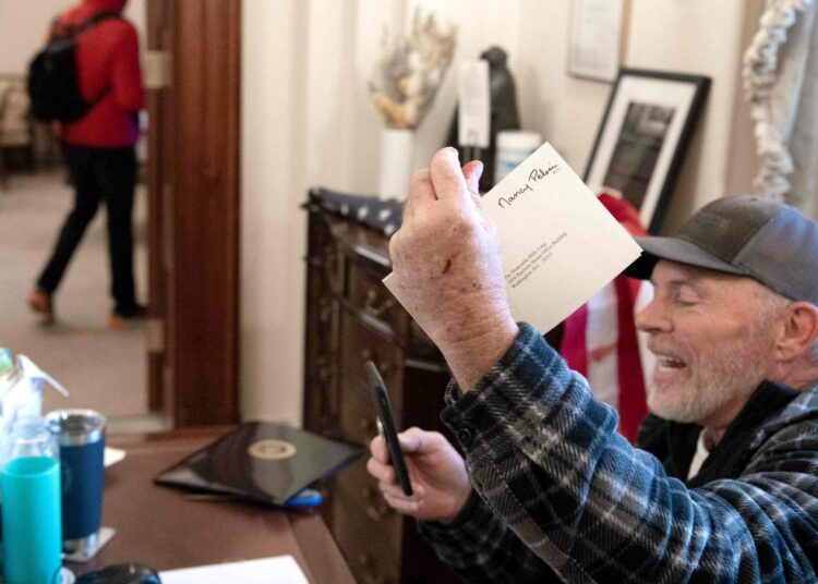 Donald Trumpin kannattaja ottamassa selfietä puhemies Nancy Pelosin toimistossa. Osa kongressin valtaajista oli varustautunut polttopulloilla ja aseilla.