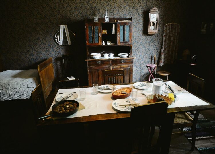 Tyypillinen viime vuosisadan alun tunnelmallinen hellahuone: Ruokapöytä keskellä, vedettävä sänky, kaappi ja seinäkello.