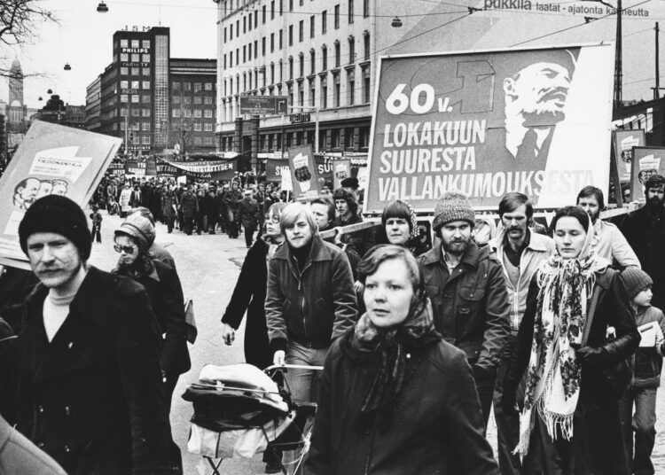 Taistolaisten tunnusmerkit vuoden 1977 vappumarssilla: Tiedonantajan mainos, kukkahuivi ja Lenin.