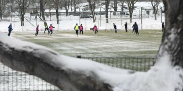Nuoria pelaamassa jalkapalloa tekonurmella lumikasojen ympäröimänä Helsingin Töölössä 18. tammikuuta.