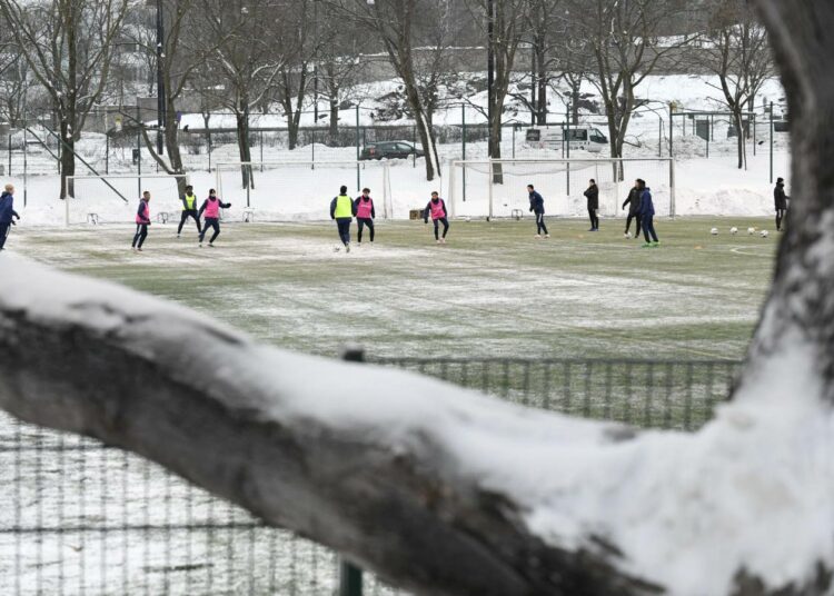 Nuoria pelaamassa jalkapalloa tekonurmella lumikasojen ympäröimänä Helsingin Töölössä 18. tammikuuta.