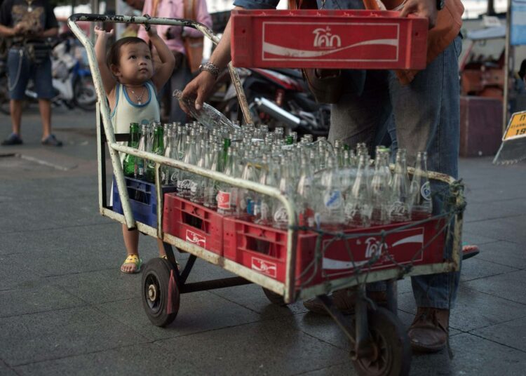 Pikkulapsi auttaa isäänsä keräämään tyhjiä pulloja Bangkokissa.