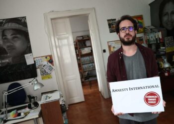 Amnestyn Unkarin osaston Aron Demeter näyttää julistetta, jonka hallituspuolue Fideszin nuorisojärjestö oli laittanut Amnestyn toimiston ulko-ovelle. Julisteessa lukee ”Maahanmuuttoa avustava järjestö”.