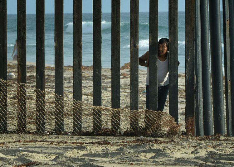 Mies katseli raja-aidan takaa Meksikon puolelta Yhdysvaltoihin San Diegossa elokuussa otetussa kuvassa.