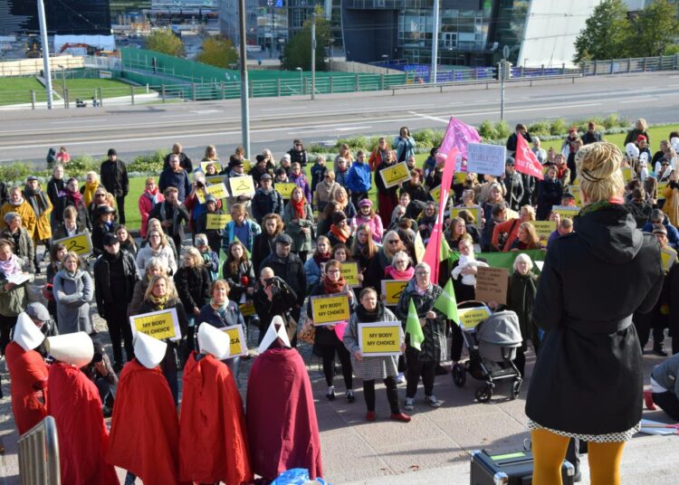 Hanna Sarkkinen (selin kameraan) puhuu mielenosoittajille Eduskuntatalon portailla.