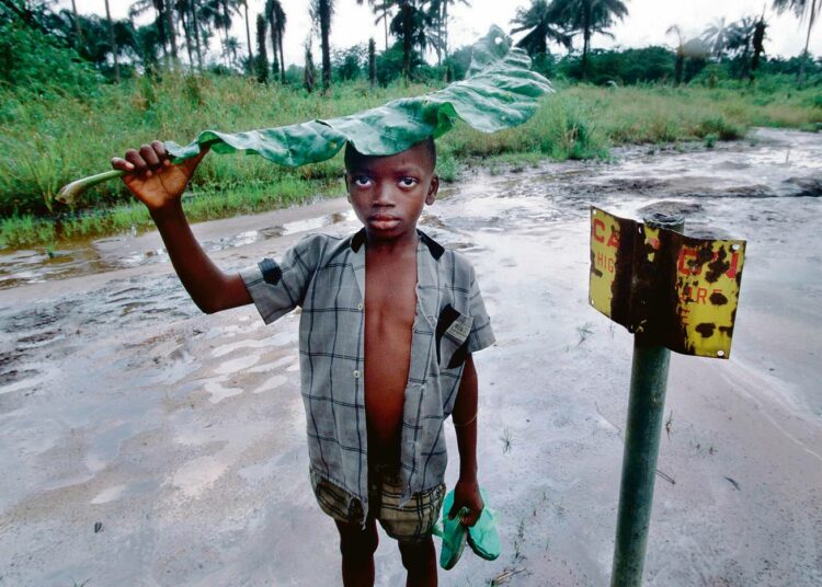 Nuori poika seisoi oljyisessä liejussa ruostuneen varoituskyltin vieressä Nigerian deltalla.