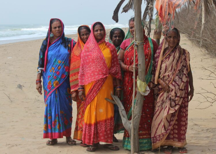 Tandaharan naiset kapealla rantakaistaleella, joka vielä erottaa kylän rajan ja alati lähestyvän meren.