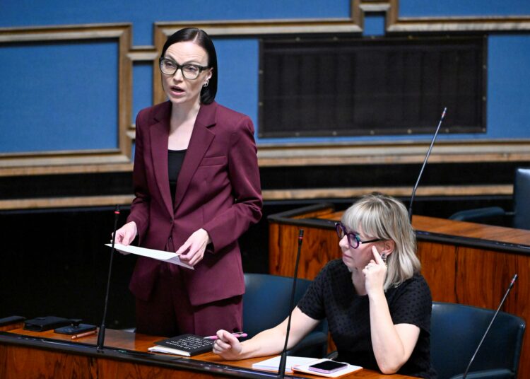 Minja Koskela (vas.) eduskunnan istuntosalissa. Istumassa Aino-Kaisa Pekonen.