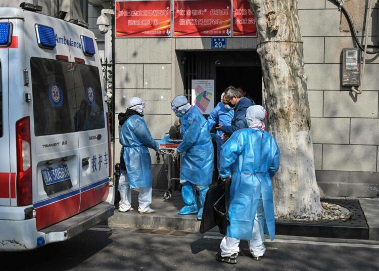 Suojapukuihin pukeutunut lääkintähenkilökunta kantaa sairastunutta ambulanssiin Kiinan Wuhanissa.