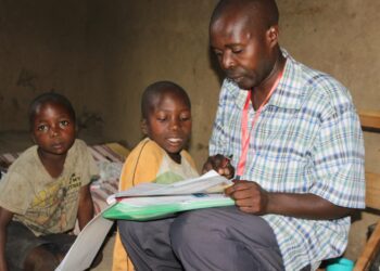 Isä auttaa lapsiaan kotitehtävissä, jotka löytyvät Education Cannot Wait -rahaston ugandalaisten kumppanien kouluihin toimittamista opetuspaketeista.