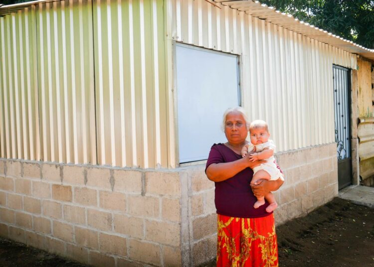 56-vuotias Gladys Reyes pitelee sylissään lapsenlastaan Emilyä talon edessä, jota laajennettiin Santo Tomásin kahvitilan tuotoilla. Tila toimii kansainvälisen Reilun kaupan järjestelmän mukaisesti El Salvadorin länsiosassa. ”Aiempi tila kävi ahtaaksi. Apu uuden osan rakentamiseen on ollut meille suuri etu”, Reyes sanoo.
