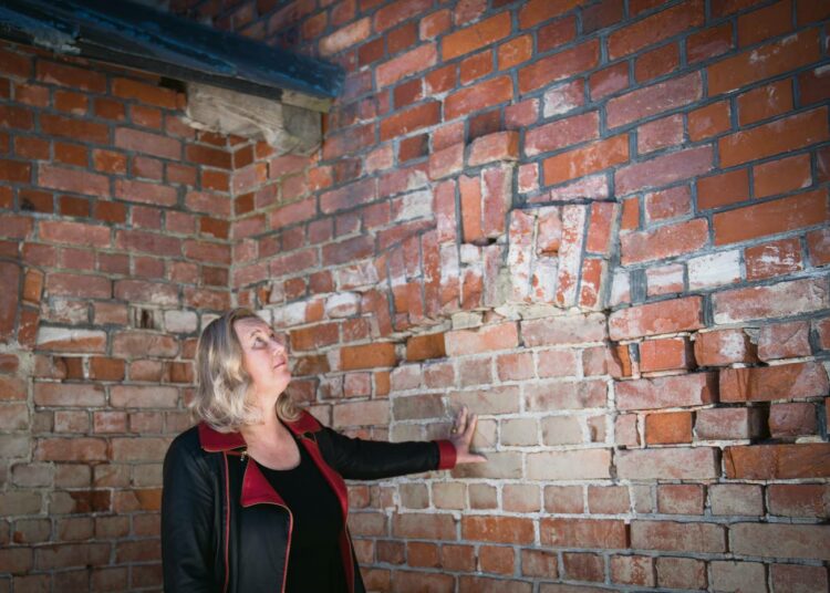 Väitöskirjatutkija Marjo Liukkonen tarkastelee luodiniskemiä koloja varastorakennuksen seinässä, jota vasten teloitettavat seisoivat.