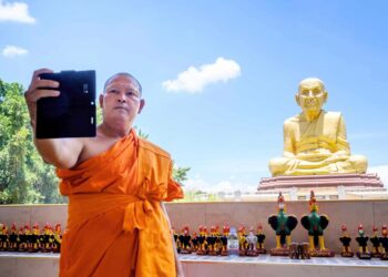 Buddhalainen munkki ottaa selfietä 1600-luvun kuuluisan munkin Luang Pu Thuatin patsaan luona Thaimaan Ayutthayassa.