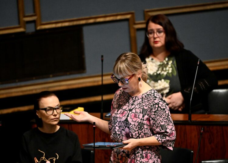Vasemmistoliiton kansanedustajia eduskunnassa: Aino-Kaisa Pekonen puhuu seisten, vasemmalla Minja Koskela ja takana Pia Lohikoski seuraavat.