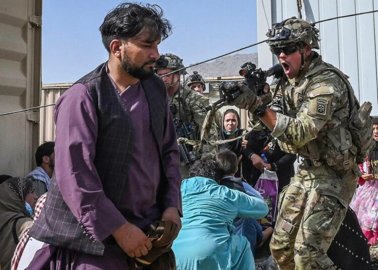 Kabulin lentokentän kaaoksessa yhdysvaltalaissotilas osoittaa aseellaan afganistanilaismatkustajaa.