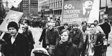 Taistolaisten tunnusmerkit vuoden 1977 vappumarssilla: Tiedonantajan mainos, kukkahuivi ja Lenin.