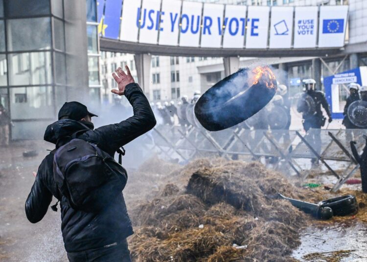 Protestoija heittää palavan autonrenkaan poliisia kohti maanviljelijöiden ammattiliiton mielenosoituksessa Brysselissä 1. helmikuuta 2024.