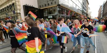 Helsinki Pride -kulkue Aleksanterinkadulla. Mukana sateenkaaren värien lisäksi myös vaaleansini-vaaleanpuna-valkoinen trans-lippu.