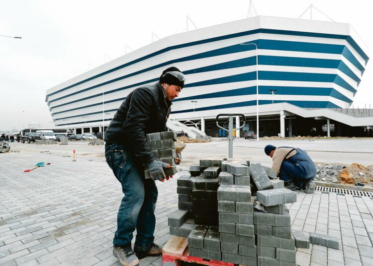 Miehet asettelivat viime viikolla katutiiliä Kaliningradin upouuden stadionin edustalle. Kisapaikkojen rakentamisessa on käytetty suurta siirtotyöläisten joukkoa.