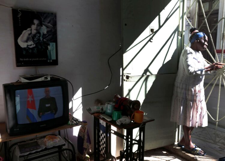 Havannalainen nainen seisoo asuntonsa ovella samalla kun presidentti puhuu televisiossa.