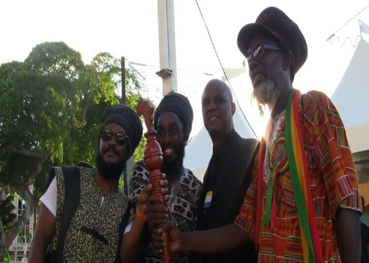 Ras Bongo Wisely Tafari (oik.) pitelee käsissään orjuuskorvausliikkeen symbolia, korvaussauvaa.