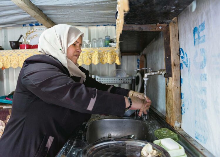 Syyrialaisnainen kotinsa keittiössä. Pakolaisperheet asuvat leirillä vaatimattomissa konttiasunnoissa. Tässä yhden huoneen ja keittiön kodissa asuu viisihenkinen perhe.