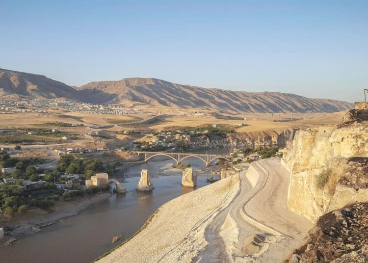 Hasankeyf ylhäältä kalliolinnakkeelta nähtynä. Kolme pilari Tigrisjoessa ovat jäänne sillasta, joka aikoinaan oli maailman pisin keskiaikaisen silta. Kauemmaksi rannasta on rakennettu uusi asuinalue, joka ei jää patoaltaan veden alle.