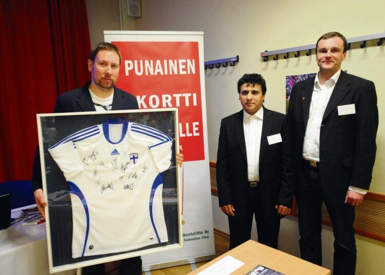 FIMU:n puheenjohtaja Mourad Bentaleb ja jalkapalloilijoiden pelaajayhdistyksen toiminnanjohtaja Markus Juhola luovuttivat Paavo Arhinmäelle maajoukkuepelaajien signeeraamaan maajoukkuepaidan.