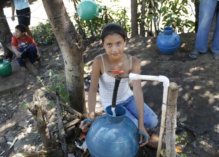 Maaseudulla El Salvadorin länsiosissa sijaitsevassa Los Pinosin kylässä asuva tyttö täyttää astiaansa maksuttomalla vesipisteellä.