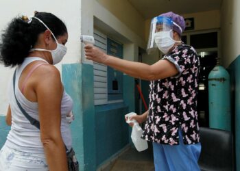 Sairaanhoitaja mittaa lämmön naiselta, joka on tulossa poliklinikalle Havannassa. Kuuban koronatilanne paheni hälyttävästi vuodenvaihteen jälkeen.