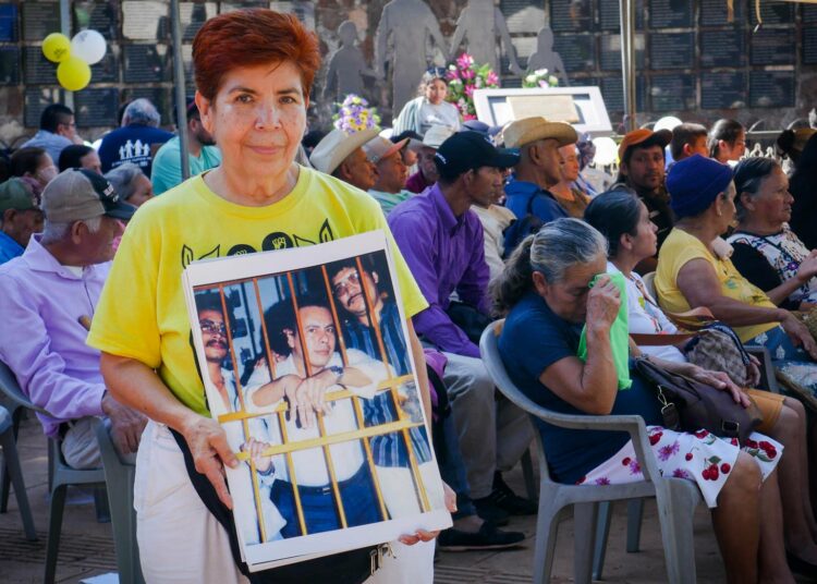 Entinen tuomari Mirna Perla El Mozoten uhrien muistotilaisuudessa. Kyltissä on kuva hänen miehestään ihmisoikeusaktivisti Herbert Anayasta, joka murhattiin lokakuussa 1987 sisällissodan aikana.
