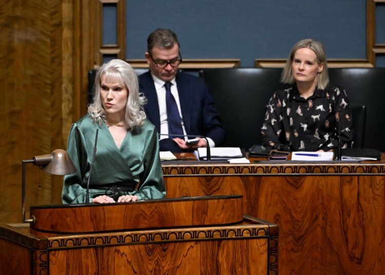Vasemmistoliiton Jessi Jokelainen puhuu, pääministeri Petteri Orpo (kok.) ja valtiovarainministeri Riikka Purra (ps.) kuuntelevat.