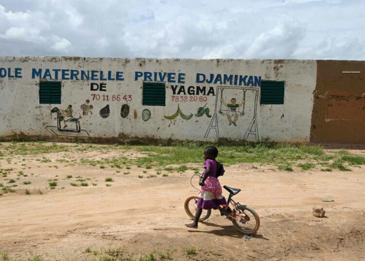 Tyttö pyöräilemässä koulun edustalla Burkina Fasossa.