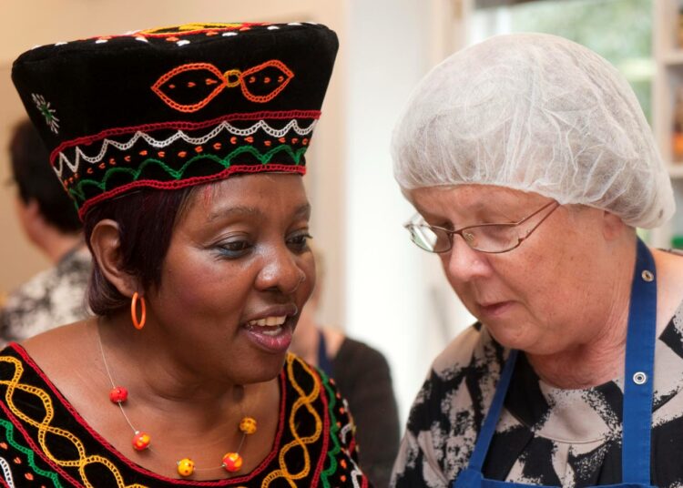 Marja Vartion hiuksia suojaa myssy, Elisabeth Domatob on pukeutunut ompelemaansa ja kirjailemaansa länsi-kamerunilaiseen juhla-asuun. Perinteisillä asuilla on monia merkityksiä. Kirjailuista, mallista ja väristä voi lukea mistä päin maata asun kantaja on kotoisin tai mikä hänen asemansa on. –¿Meille nämä asut kertovat itsekunnioituksesta, että olemme ylpeitä juuristamme.