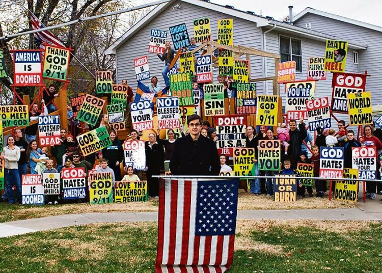 Kylteistä: ”Jumala vihaa Amerikkaa”, ”Jumala vihaa sinua”, ”Kiittäkää Jumalaa 9/11-terrori-iskuista”. Kuvassa etualalla toimittaja Louis Theroux.