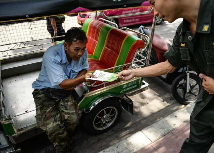 Varusmies ojentaa tuk-tuk-kuljettajalle lehtisen, jossa kerrotaan tulevasta perustuslakikansanäänestyksestä.