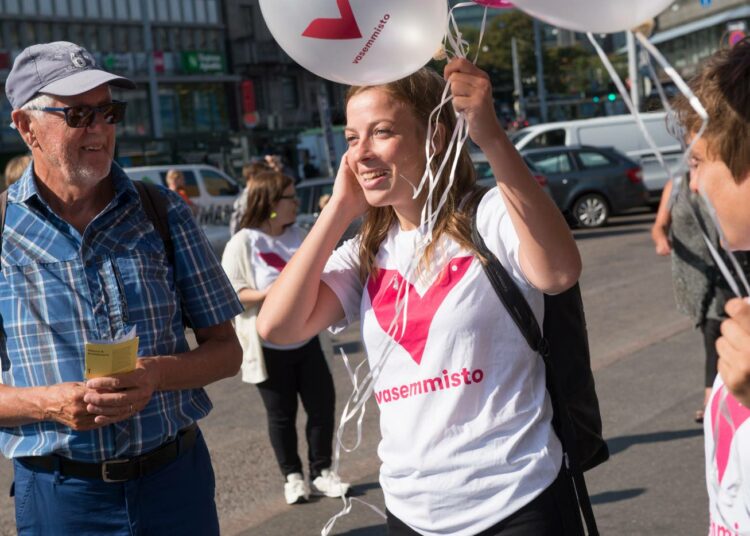 Li Andersson jakamassa Vasemmistoliiton uudella logolla varustettuja ilmapalloja elokuussa Helsingin Rautatieasemalla.