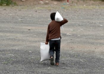 Pandemian aiheuttama muutos saattaa YK:n mukaan suistaa 265 miljoonaa ihmistä nälänhätään. Kuvassa jemeniläispoika kantaa perheen avustusruokasäkkejä.