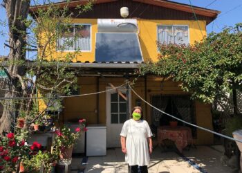 Peruskoulun opettaja Marta Pérez seisoo talonsa edustalla, takanaan seinällä aurinkolämpöpaneeli, joka on jälleen mahdollistanut kuumasta vedestä nauttimisen. Hänen perheellään ei ollut varaa käyttää sähköllä toimivaa vedenlämmitintä, sillä sähkö on niin kallista.