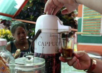 Tarjoilija kaataa kahvia lasiin kahvilan edustalla Havannan Vedadon naapurustossa. Kahvinjuonti kadulla ja kodissa on kuubalainen tapa, jonka ylläpito on muuttunut yhä työläämmäksi saatavuusvaikeuksien ja korkean hinnan vuoksi.
