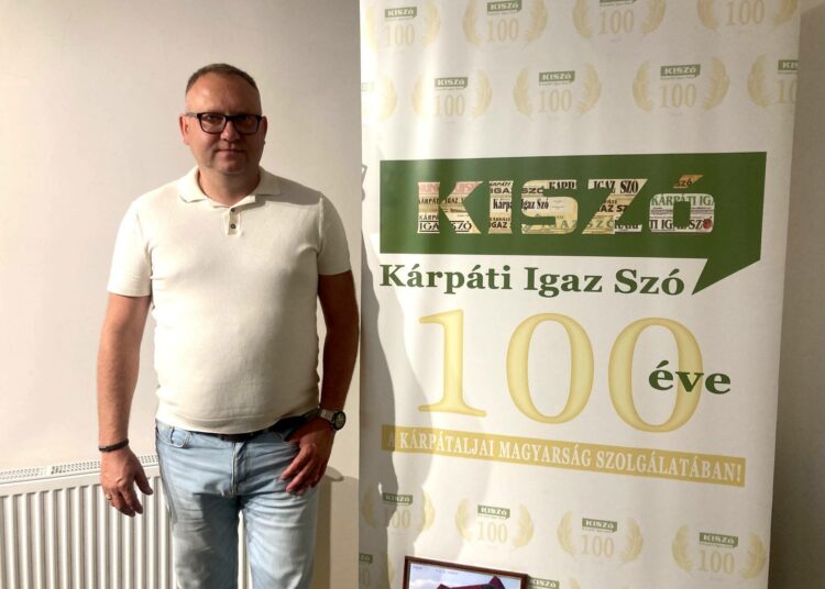 György Dunda seisoo Kárpáti Igaz Szó -lehden satavuotispäivän kunniaksi tehdyn julisteen vieressä. Länsi-Ukrainan Taka-Karpatiassa ilmestyvä unkarilainen viikkolehti tarvitsee Budapestin taloudellista tukea.